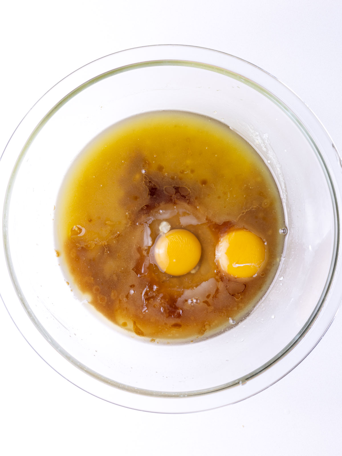 Egg, egg yolk, and vanilla added to the butter and sugar mixture in the clear glass mixing bowl.