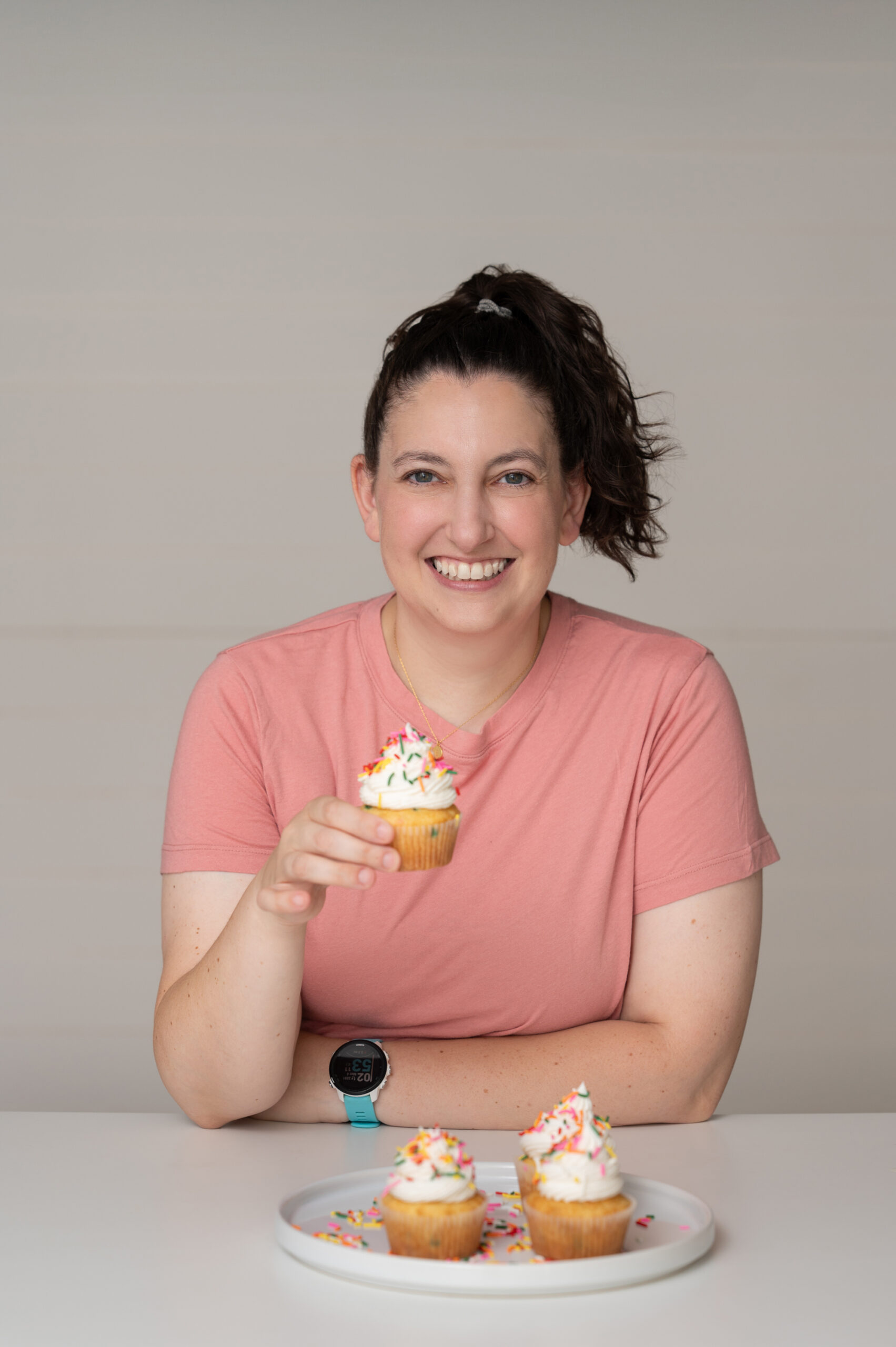 Liz wearing a pink shirt and holding a funfetti cupcake.