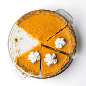 A sliced sweet potato pie with one slice removed and dollops of whipped cream on the sliced pieces.