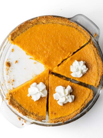 A sliced sweet potato pie with one slice removed and dollops of whipped cream on the sliced pieces.