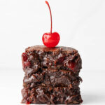 A stack of three fudgy chocolate cherry brownies with a maraschino cherry on top.