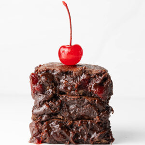 A stack of three fudgy chocolate cherry brownies with a maraschino cherry on top.